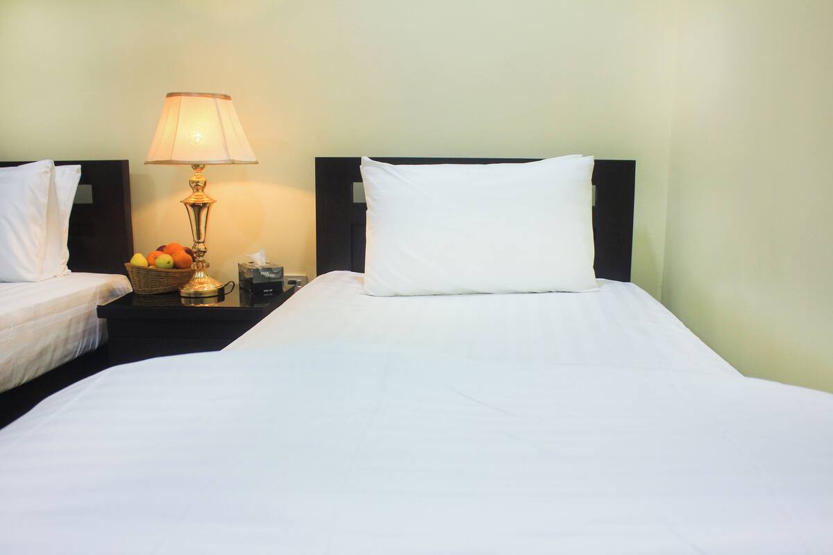 Une chambre d’hôtel avec deux lits, une table de chevet avec une lampe et un panier de fruits.