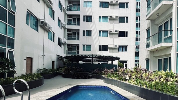 A swimming pool surrounded by a modern building with multiple balconies and a covered outdoor seating area. - Room-staycation Champ Close to Your Hear (Iloilo)
