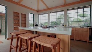 Una cocina amplia con una isla grande, taburetes de madera y vistas al exterior.