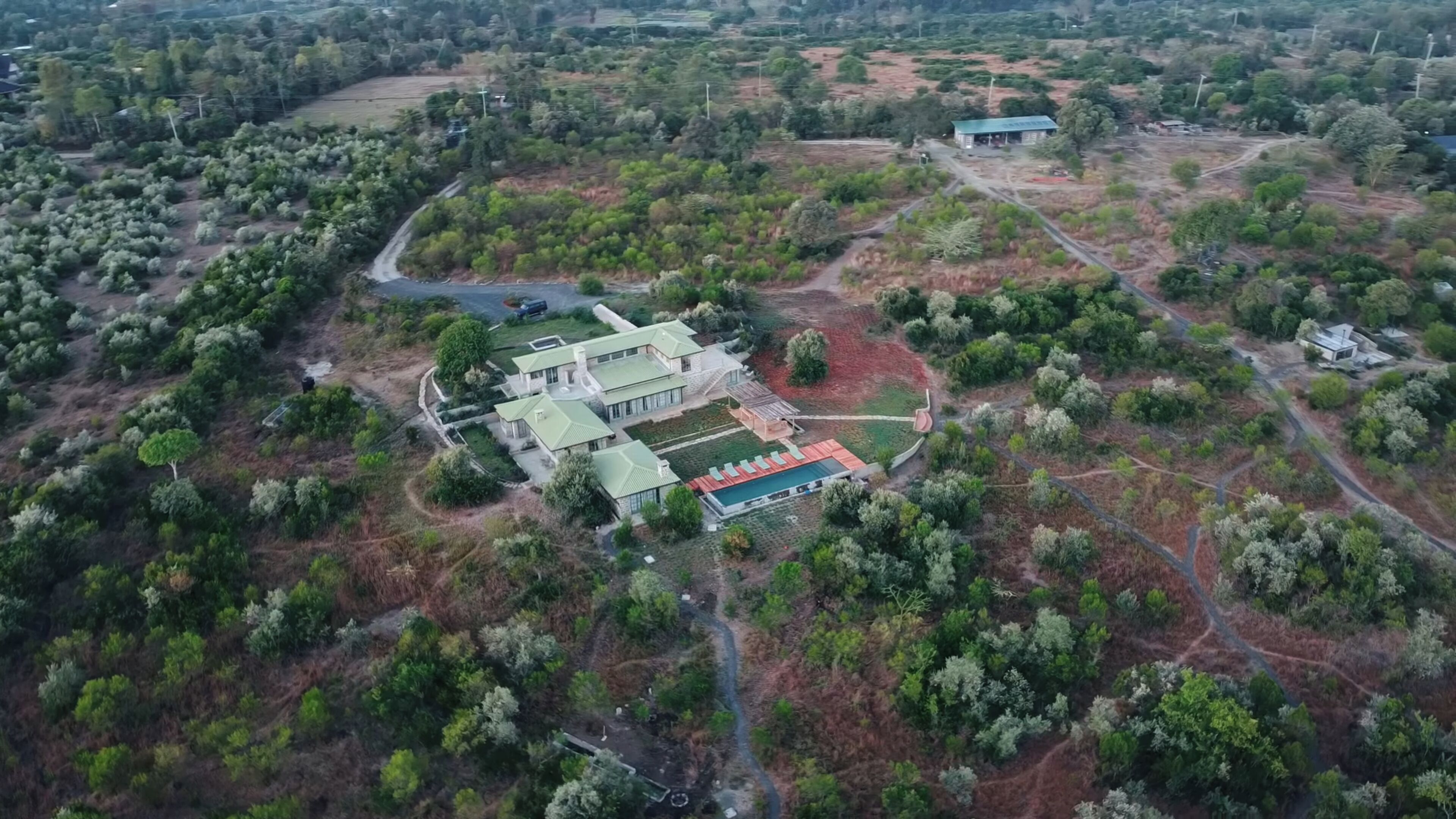 Vista aérea de uma grande propriedade com vários edifícios, jardins extensos e piscina.