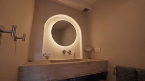 Une salle de bain avec un grand miroir ovale, un lavabo, un petit miroir rond et un porte-serviettes.