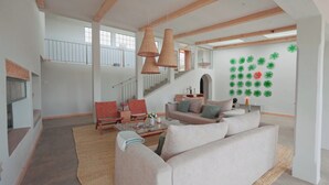 Amplia sala de estar con techo alto, vigas de madera, una escalera y una pared decorada con adornos circulares verdes.