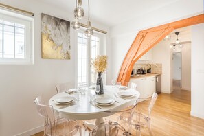 Ein Essbereich mit einem runden Tisch, gedeckt für sechs Personen, klaren Stühlen und einer Vase mit getrockneten Pflanzen.