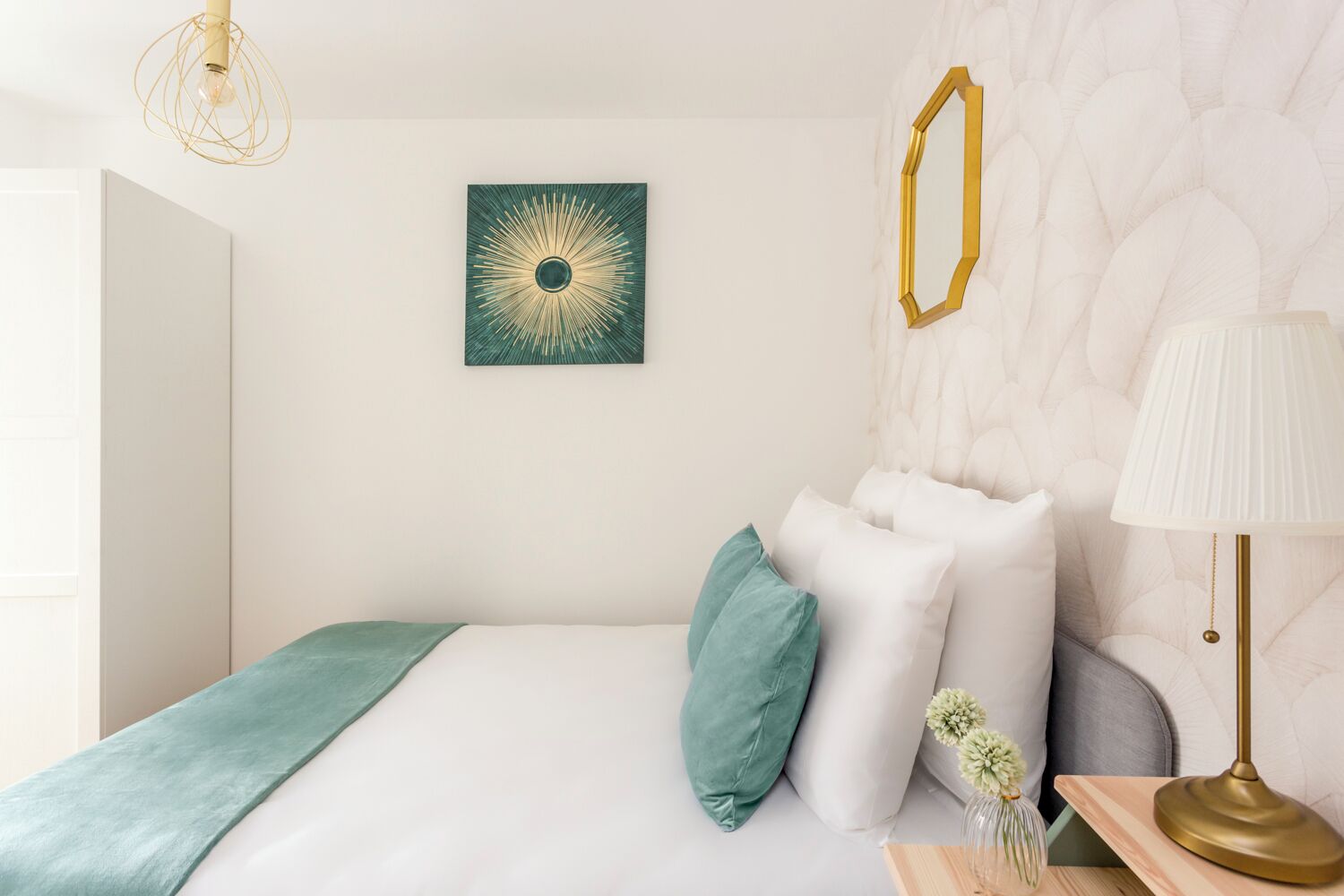 A modern bedroom with a bed, pillows, a wall-mounted mirror, a lamp, and a decorative wall piece.