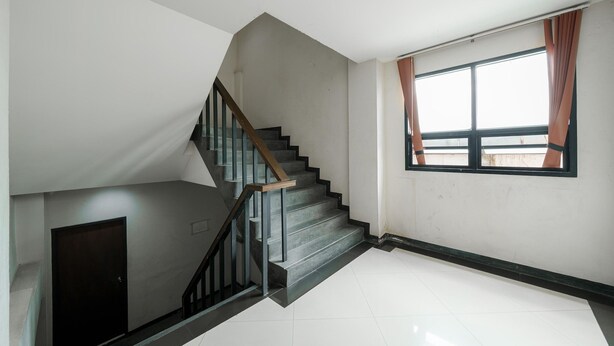Eine Treppe mit hölzernem Geländer und schwarzen Metallstreben, die zu einer Empore mit einer geschlossenen Tür führt.