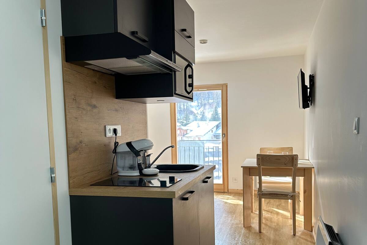 Une cuisine moderne avec des meubles de couleur noire, une cuisinière encastrée et une table à manger en bois, accompagnée d’une chaise.
