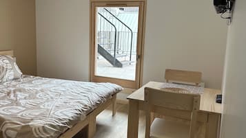 Un dormitorio con una cama, un escritorio de madera, una silla, una ventana con vista a una escalera y un televisor montado.