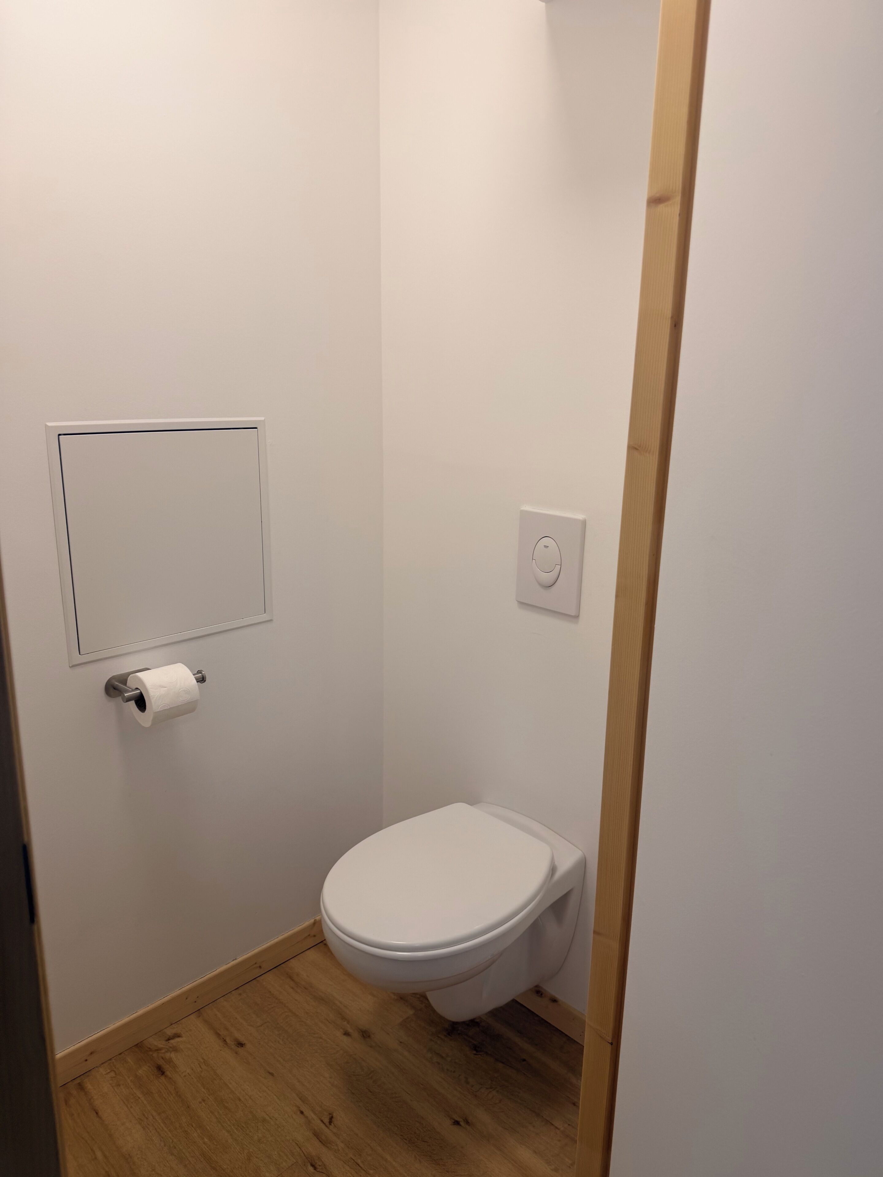 A small, clean bathroom with a toilet, a toilet paper holder, and a light switch on the wall.