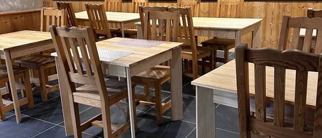 Un restaurante con mesas y sillas de madera, una zona de cocina con electrodomésticos y un suelo de baldosas.