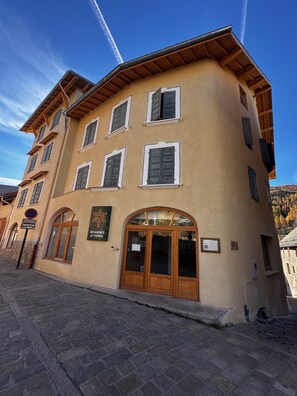 A multi-story building with a beige facade, wooden shutters, and a large arched entrance. - residence le prorel (Saint-Chaffrey)