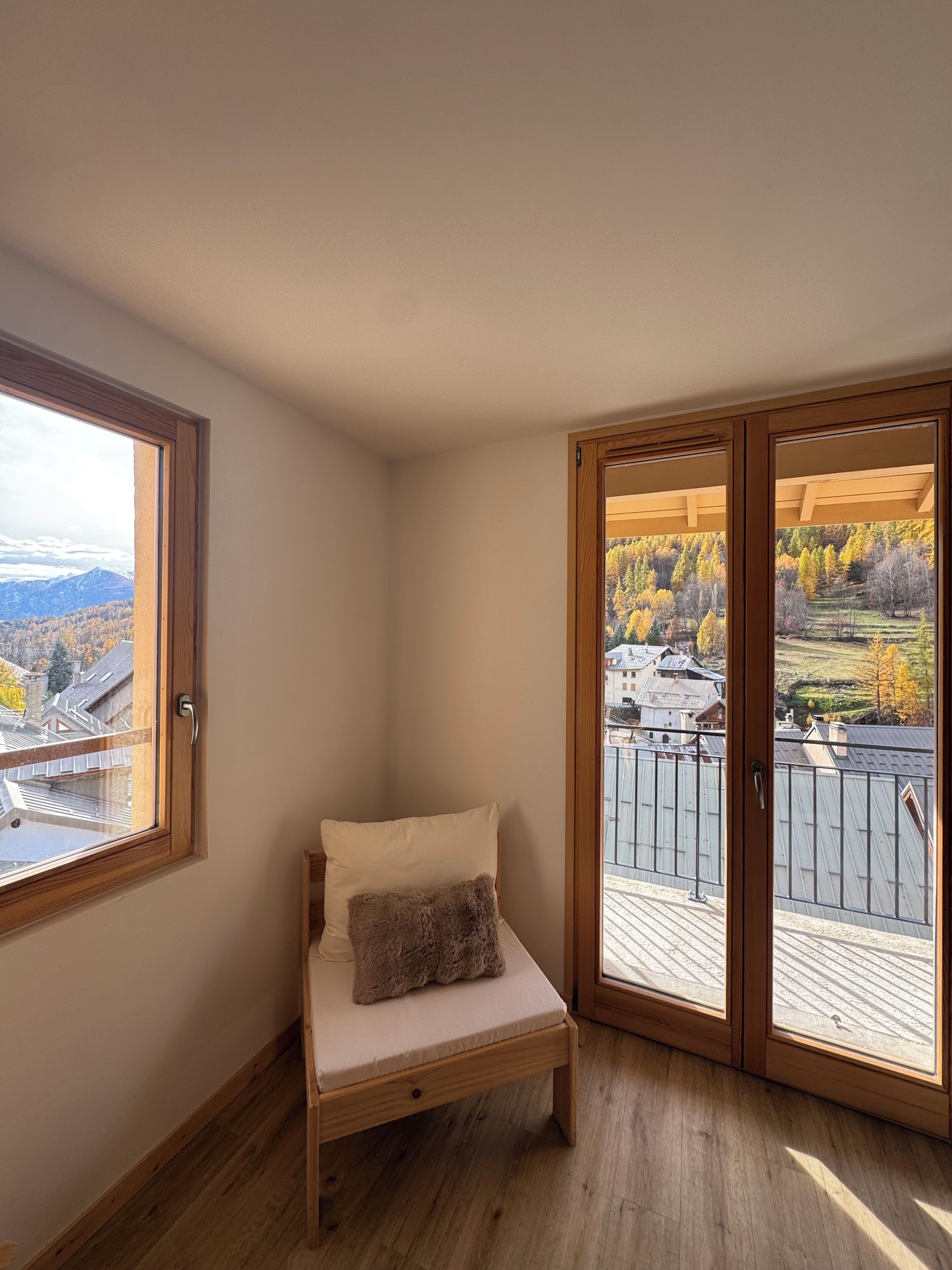 Dormitorio en esquina con un banco de madera, una almohada y vistas a un balcón con barandilla.