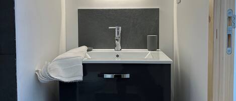 A modern bathroom with a white sink, dark cabinet, and a mirror with integrated lighting.