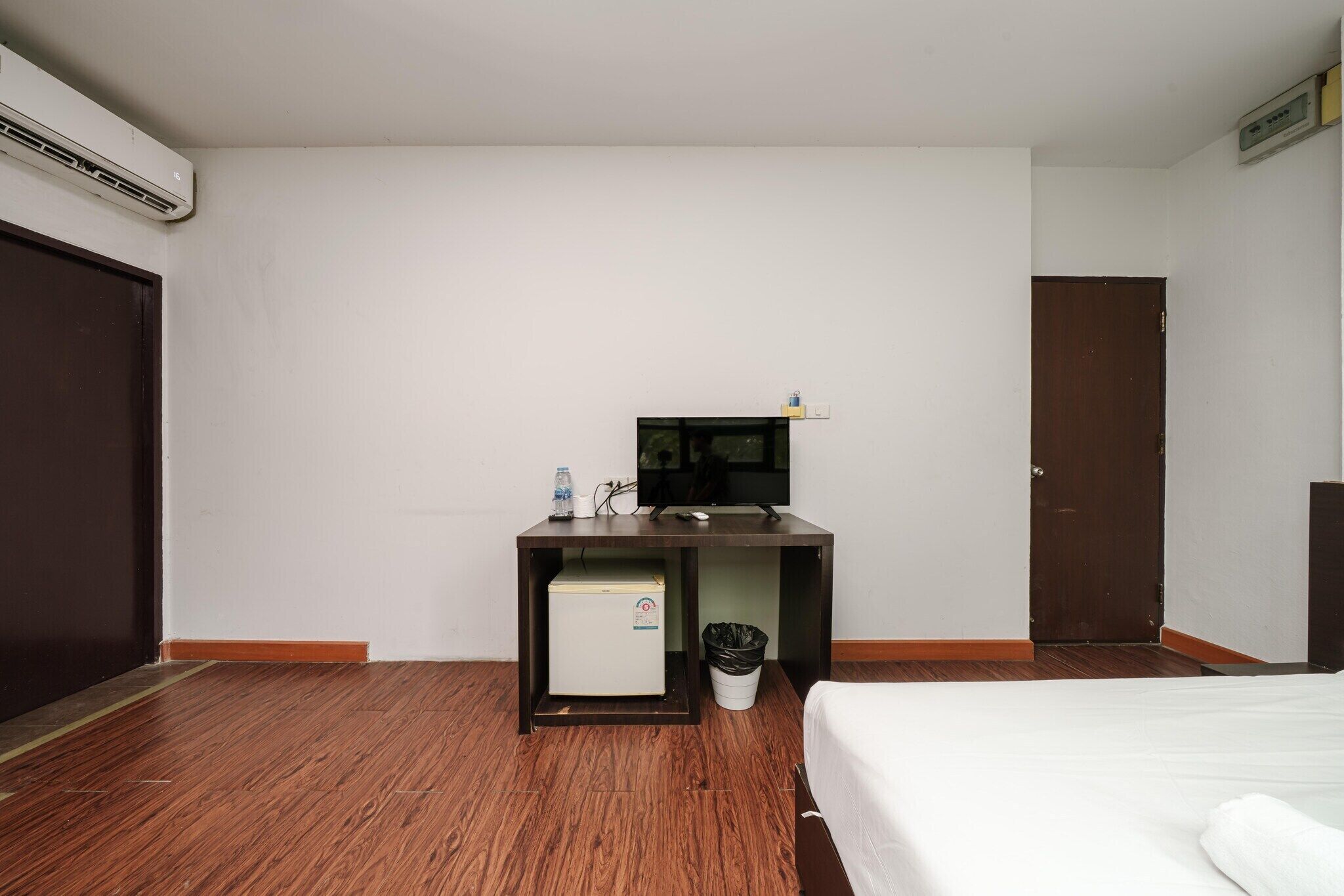 Une chambre d’hôtel comprenant un lit, un bureau avec un ordinateur, un petit réfrigérateur, une poubelle et une porte.