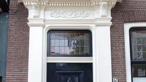 Una puerta negra con diseños intrincados, un marco decorativo blanco y un ventanal encima.
