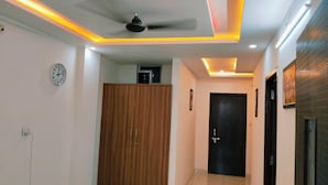 A hallway with a ceiling fan, recessed lighting, a wooden wardrobe, a clock, and a door. - Hotel Bhavya Palace (Udaipur)