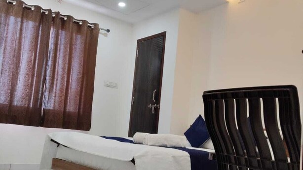 A bedroom with a bed, a chair, a ceiling fan, and a door. - Hotel Bhavya Palace (Udaipur)