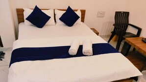 A neatly made bed with white and navy blue bedding, two navy blue pillows, and two rolled towels. - Hotel Bhavya Palace (Udaipur)