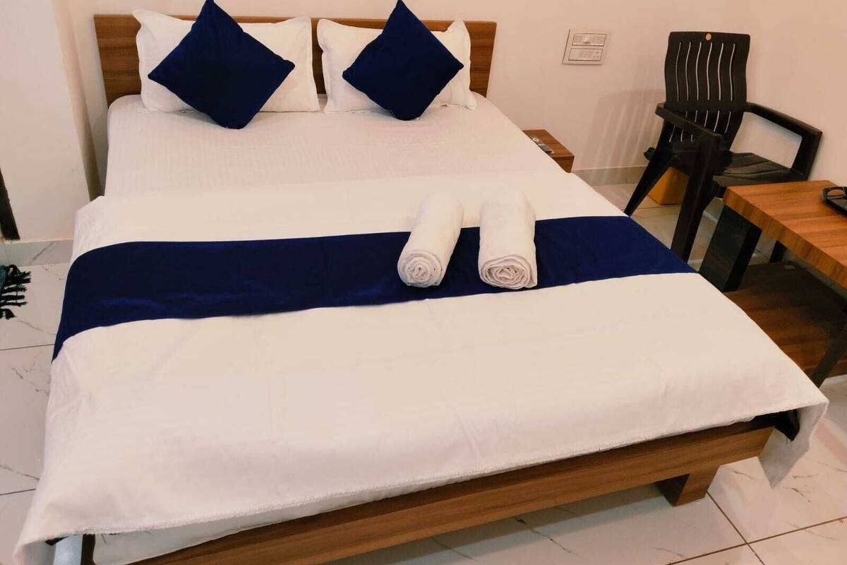 A neatly made bed with white and navy blue bedding, two navy blue pillows, and two rolled towels.