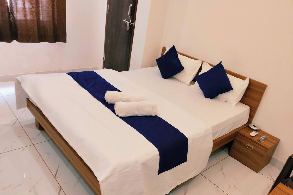 A neatly made bed with white and blue bedding, a wooden headboard, and a small bedside table with a lamp and a phone.