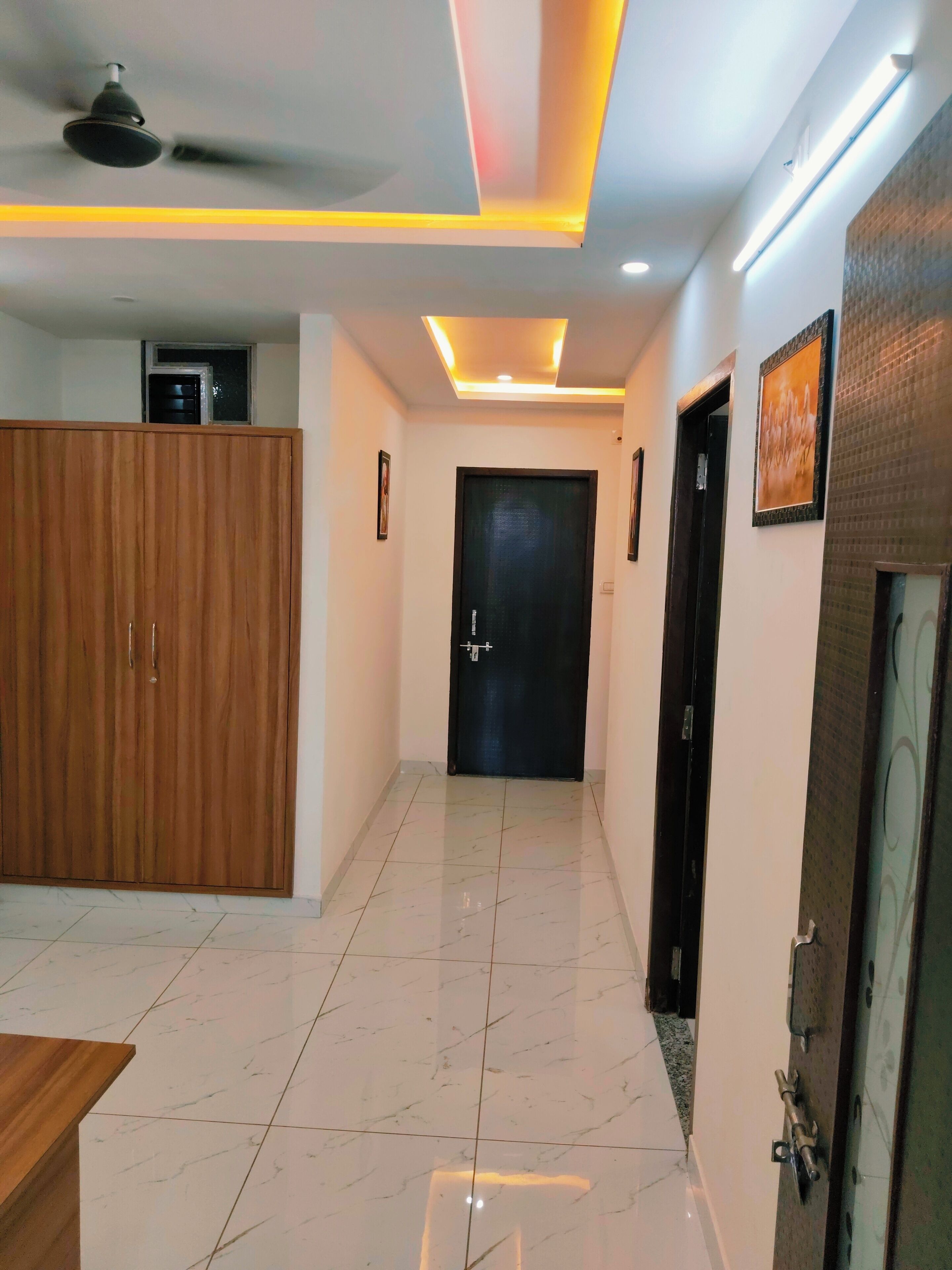 A hallway with a wooden wardrobe, a black door, and a tiled floor.