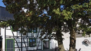 Un bâtiment traditionnel à la façade blanche et aux touches de vert, doté d’une cour avec des sièges extérieurs et un arbre.