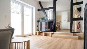 Un salon moderne avec un plancher en bois, un téléviseur posé sur un meuble, un coin repas avec une table et des chaises, et une cuisine à l’arrière-plan.