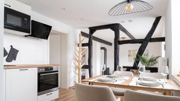 Une cuisine moderne dotée d’appareils électroménagers intégrés, un coin repas avec une table et des chaises en bois, et des poutres apparentes.