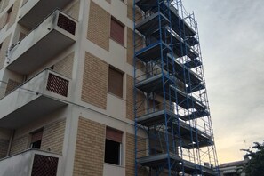 Un edificio de varios pisos con fachada de ladrillo y andamios azules a la derecha.