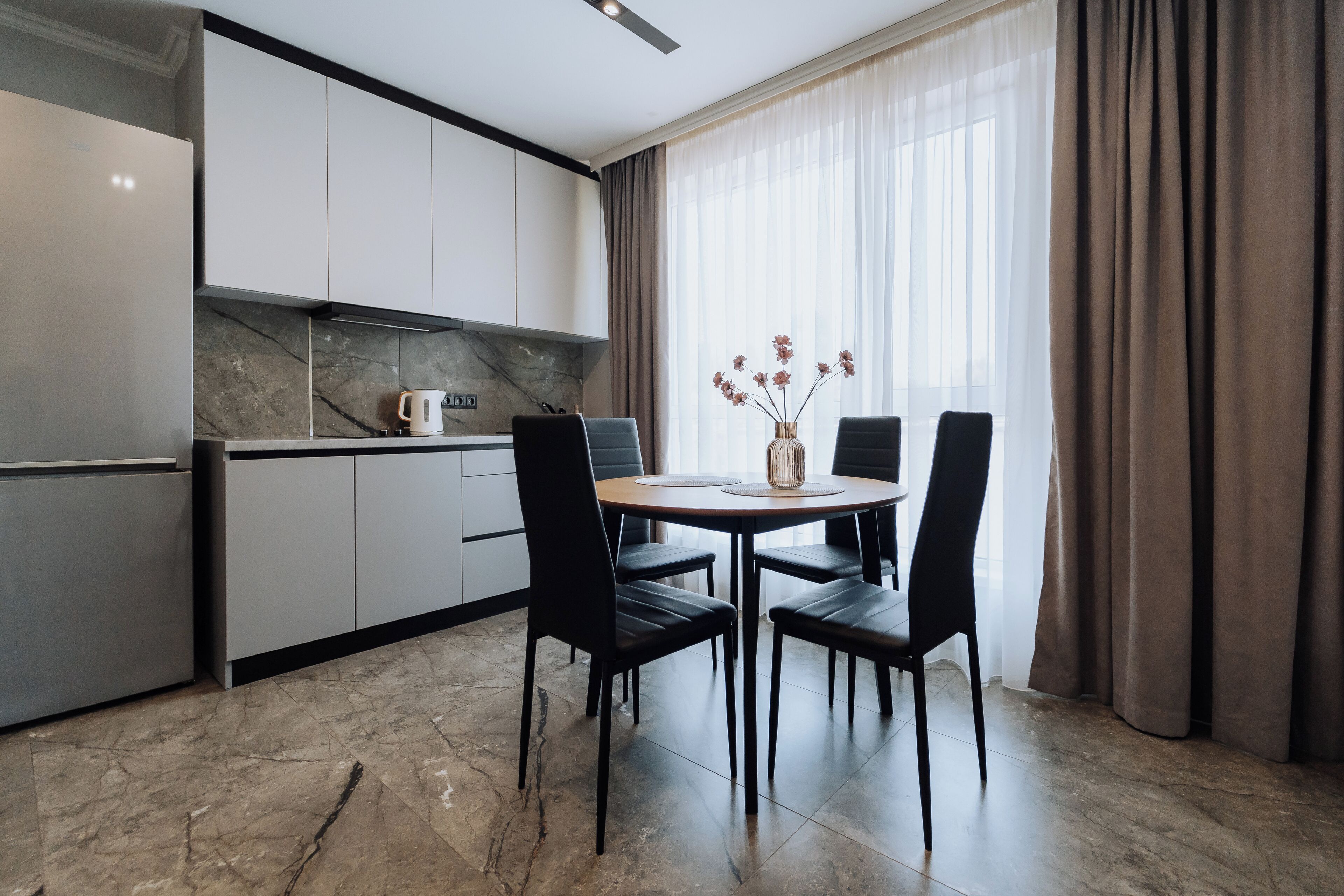 A modern kitchen with white cabinets, a marble backsplash, and a dining area with a round table and four chairs.