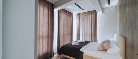 A modern hotel room with a bed, curtains, and a ceiling with recessed lighting.