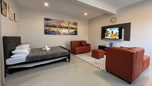 A modern hotel room with a bed, a sofa, a TV, and artwork on the walls.