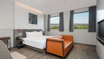 Une chambre d’hôtel avec un lit, un canapé orange, un bureau avec un téléphone et une télévision.