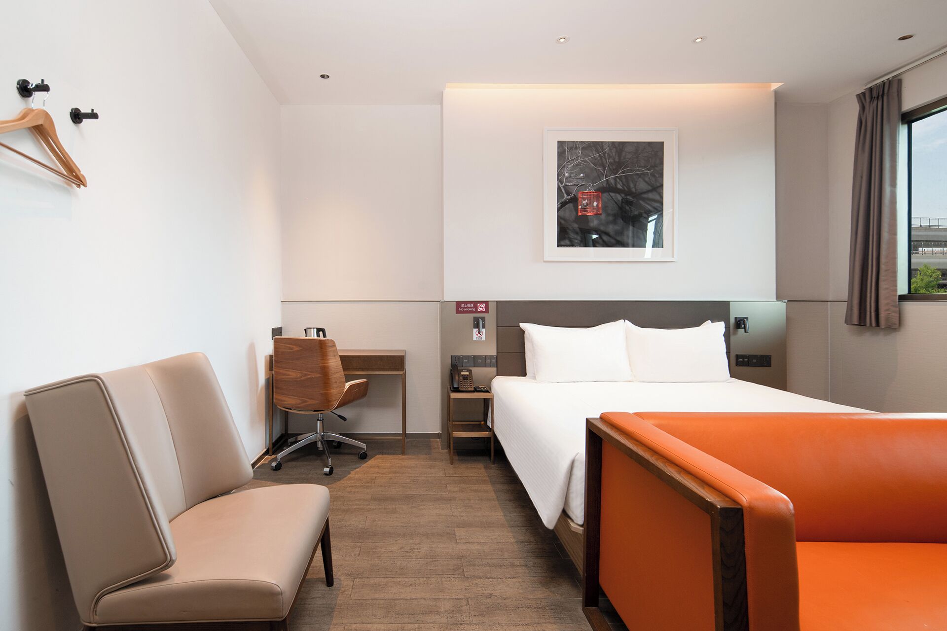 A hotel room with a bed, a desk with a chair, a sofa, and a painting on the wall.