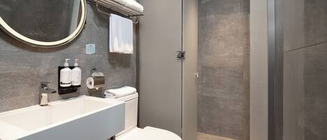 Un baño moderno con lavamanos blanco, inodoro y ducha con mampara de vidrio.