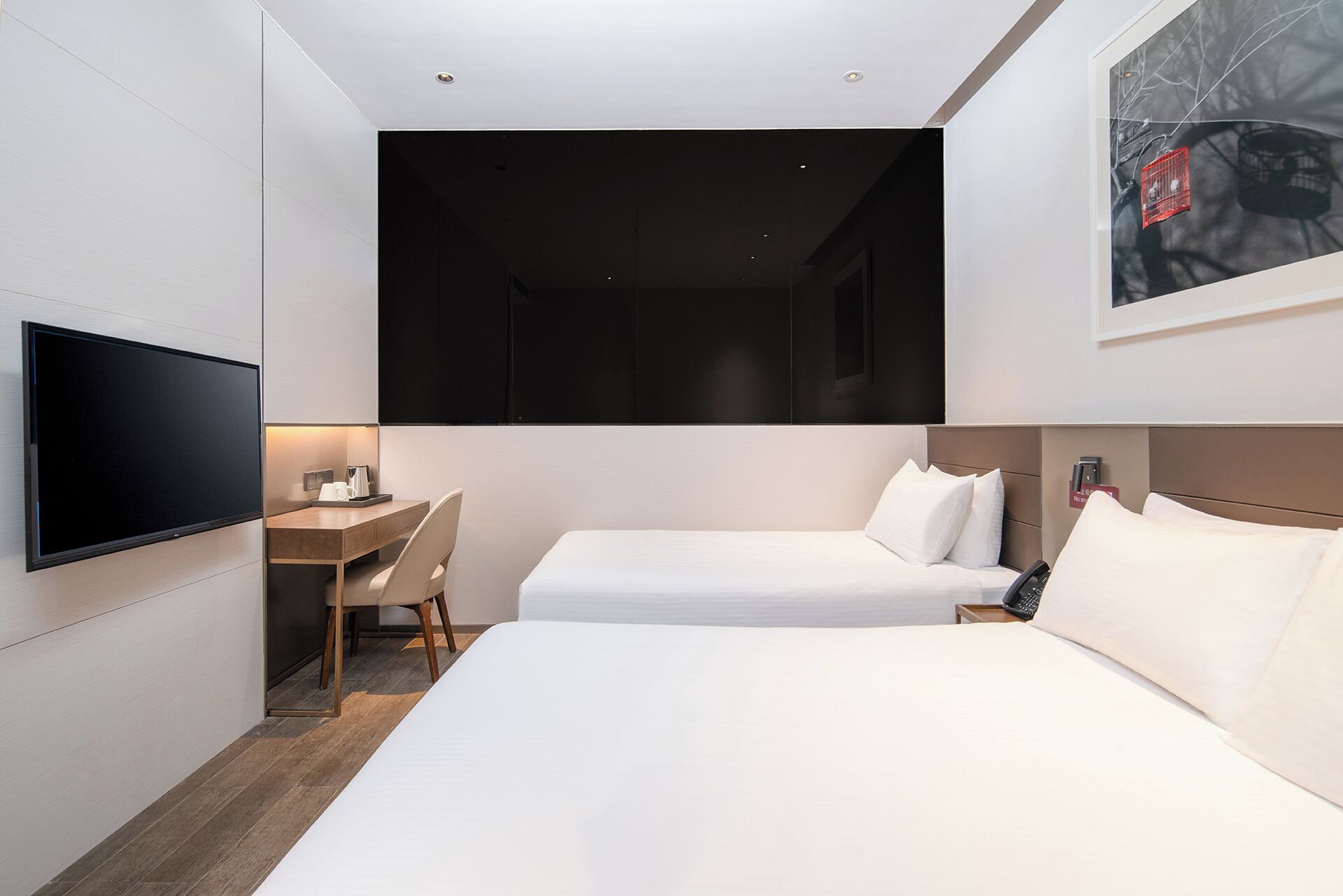 A hotel room with a flat-screen TV mounted on the wall, a desk with a chair, two beds with white linens, and a framed picture on the wall.