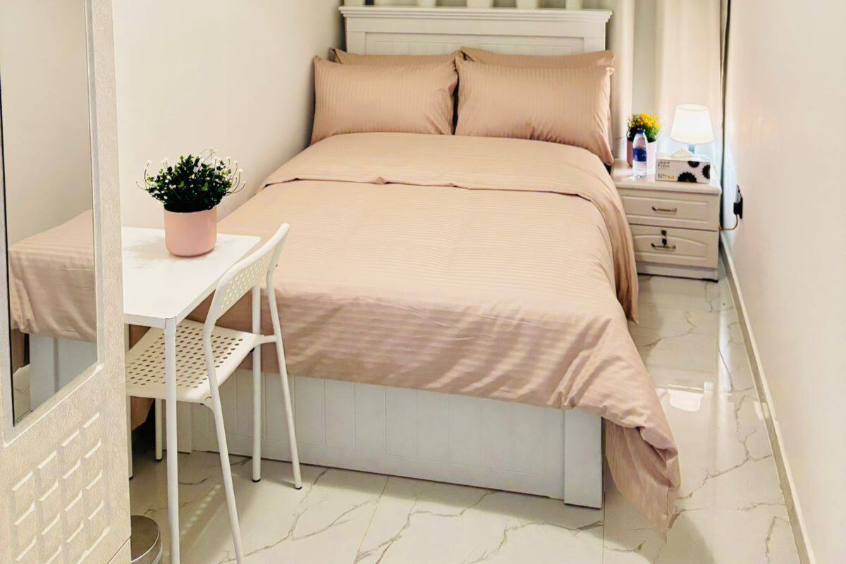 A bedroom with a bed, a bedside table with a lamp, a small potted plant, and a mirror.