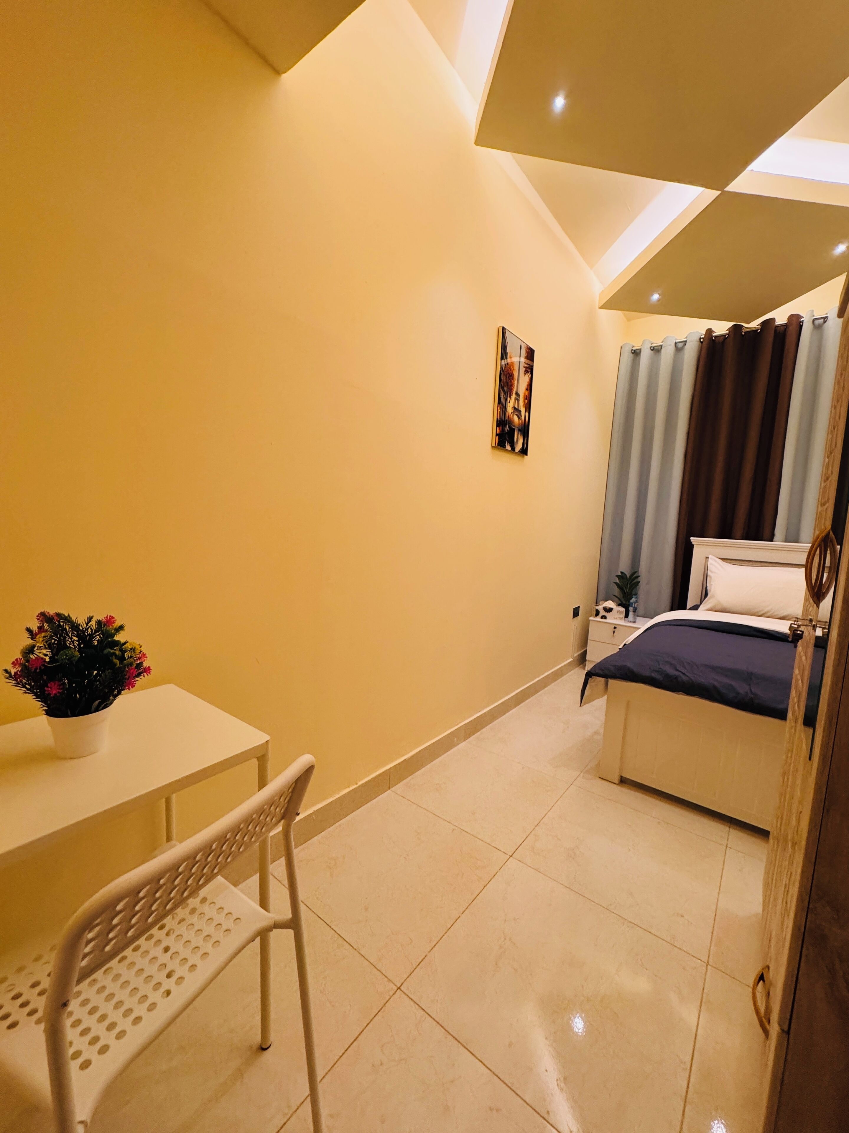 Una habitación pequeña y luminosa con una cama, un escritorio, una silla y una planta en maceta.