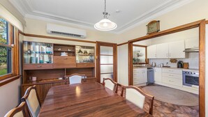 Une salle à manger avec une table et des chaises en bois, une cuisine intégrée avec des meubles blancs et une grande fenêtre.