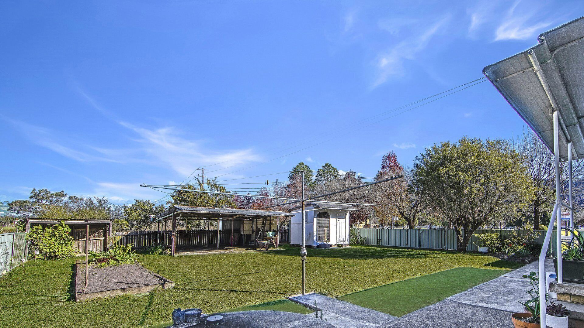 A residential backyard with a fenced area, a small shed, and a lawn.