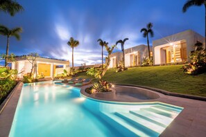 A swimming pool with a curved edge, surrounded by palm trees and a well-maintained lawn. - Asri Village Two (Pecatu)