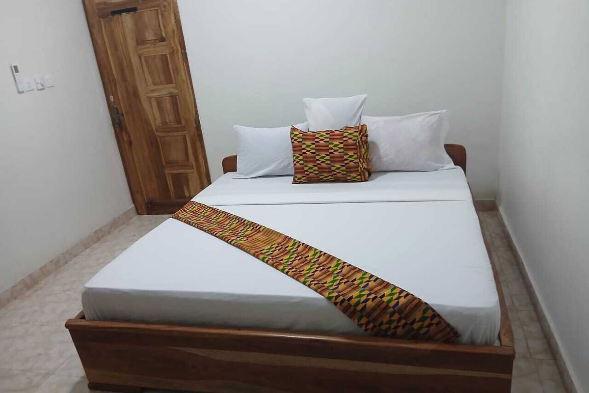 A single-bed room with a wooden frame, white bedding, and a patterned throw.