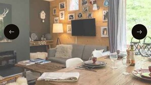 Un salón acogedor con una mesa de madera dispuesta para una comida, un sofá y un televisor de pantalla plana montado en la pared.