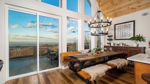 A spacious kitchen with a large dining table, wooden benches, and a view through large sliding glass doors to an outdoor deck.