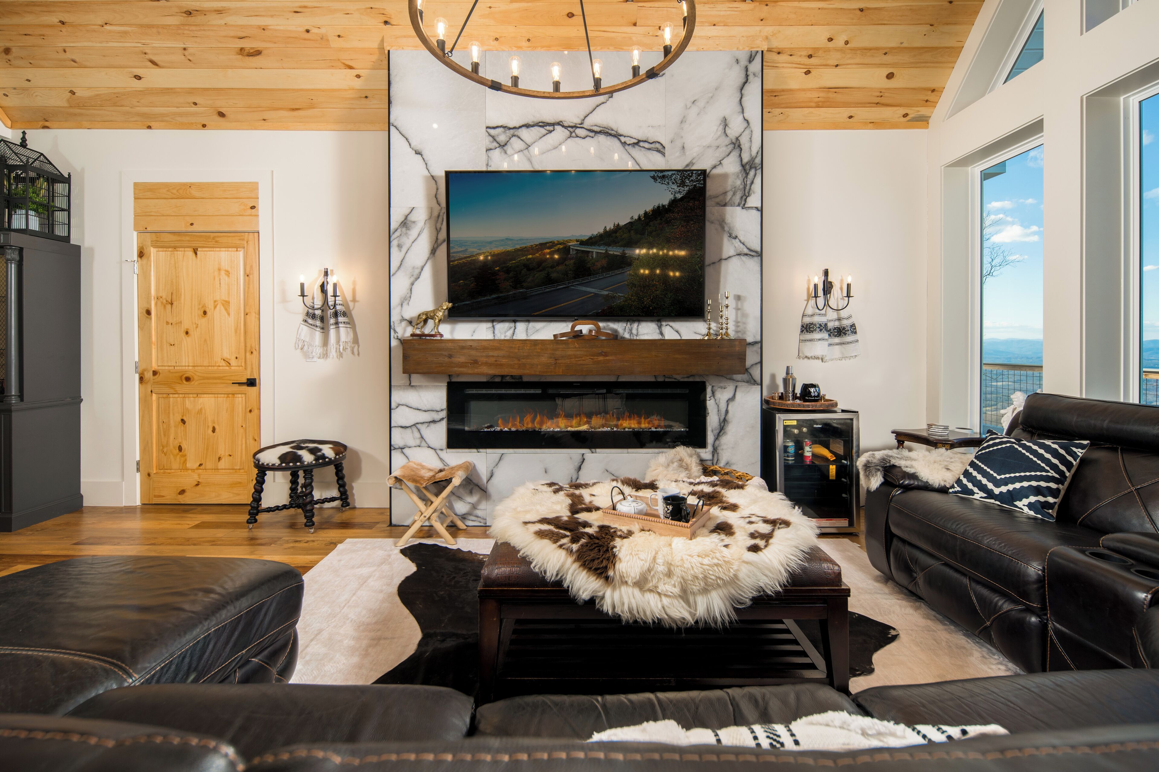 A modern living room with a fireplace, leather sofas, a mounted TV, and a wooden ceiling.