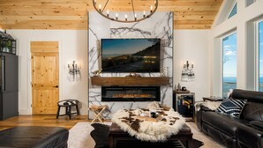 A modern living room with a fireplace, leather sofas, a mounted TV, and a wooden ceiling.