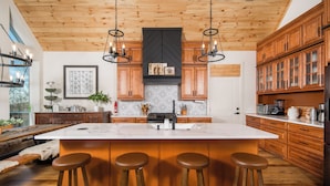 A modern kitchen with a large island, wooden cabinets, and pendant lighting.