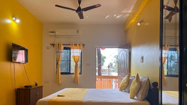 Un dormitorio con cama, televisor, aire acondicionado y balcón con barandilla.