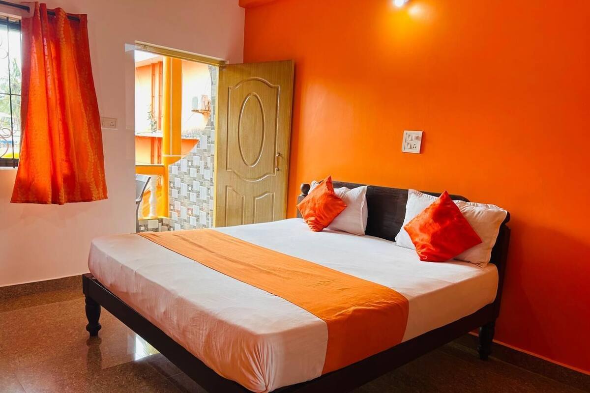 Quarto de hotel com cama, cortinas laranja, porta de madeira e vista para o exterior.