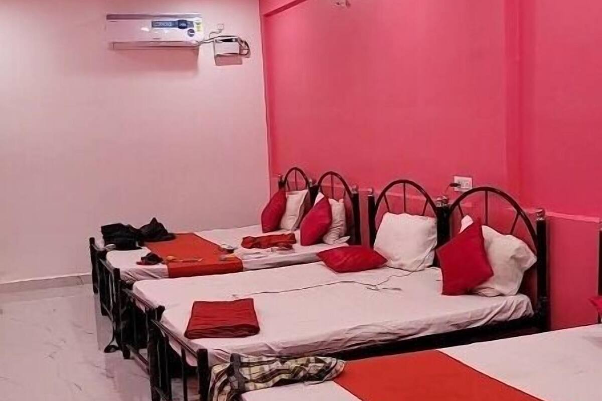 Quarto de hotel com quatro camas de solteiro, cada uma com colcha vermelha e branca, e um ventilador de teto.