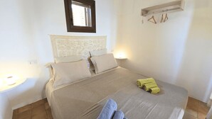 A neatly made bed with a headboard, two bedside lamps, and a window with a view. - Dammuso - Cala Cinque Denti - AFFITTI\'CA (Pantelleria)